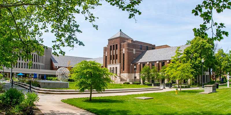 An image of Tirey Hall from across the quad during summer. Parsons Hall and the Trumpets artwork are also visible in the distance.